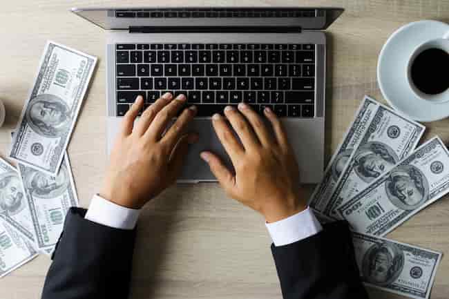 Бизнесмен, работающий с ноутбуком с долларовыми купюрами за офисным столом.